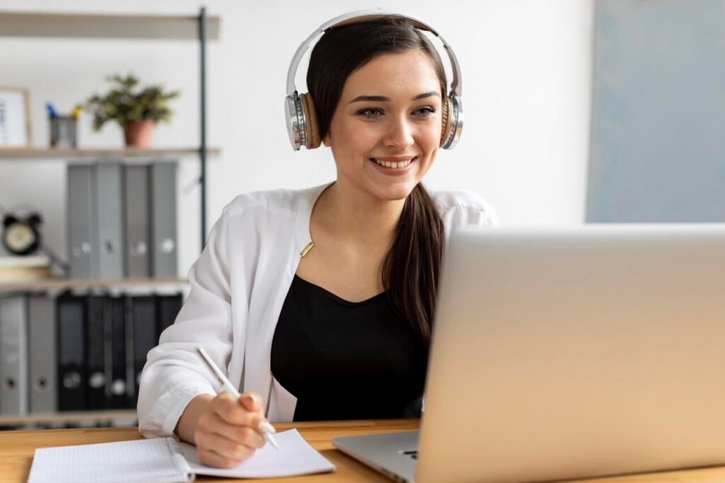 Mujer sonriente usando auriculares frente a un ordenador.